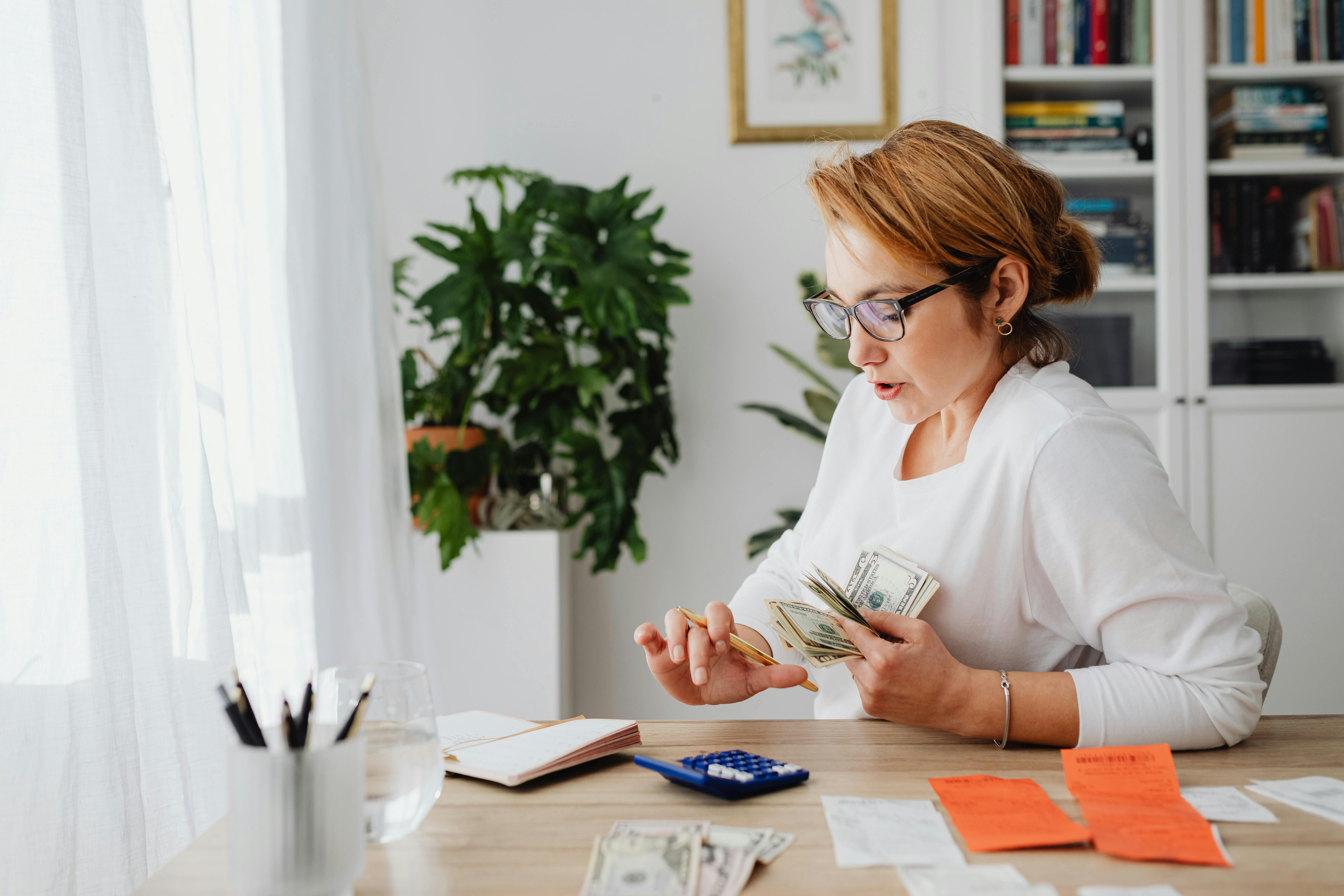 person holding money and doing calculations on a calculator